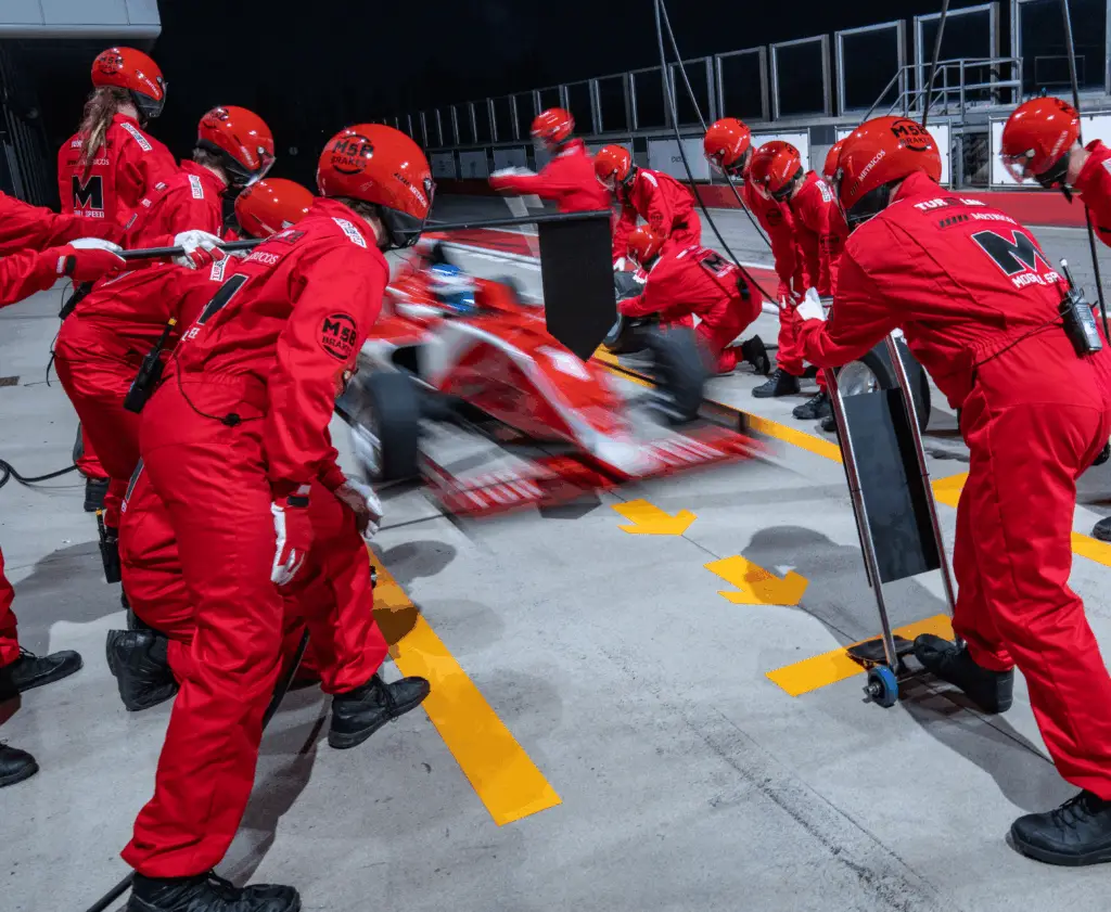 Pit crew in red uniforms rapidly servicing a race car during a pit stop.